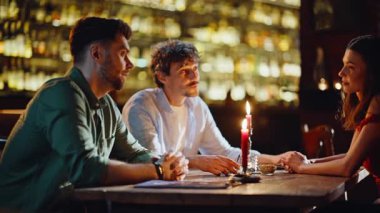 İki romantik çift, akşam yemeğinde samimi bir kafede sohbet ediyorlar. Modern restoran masasında parlayan mumlarla oturan rahat erkekler. Gülümseyen arkadaşlar bardaki gayri resmi iletişimden keyif alıyorlar.