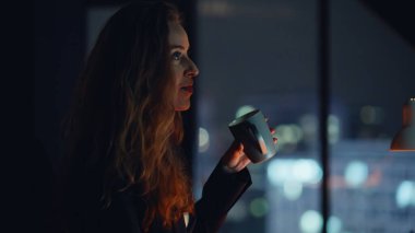 Profesyonel kadın gece ofis resmine ara veriyor. İşten sonra kahve içen, rahatlayan bir kadın. Gülümseyen yönetici masasında sükunetin keyfini çıkartıyor. İşçi çayını yudumluyor 