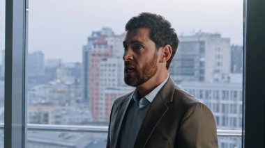 Deli müdür, şehir manzaralı ellerle hayal kırıklığını ifade ediyor. Sinirli iş adamı içeride yüksek sesle bağırıyor. Stresli sinirli adam kötü iş durumlarında ofiste duygularını gösteriyor.