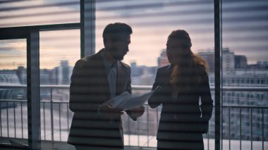 Kızgın yönetmen tartışan sekreter, büyük pencerenin önünde yakın plan. Stresli işadamı elinde saldırgan bir şekilde el kol hareketi yapan kağıtlar tutuyor. Sinirli iş kadını iş ortağıyla çelişen raporlar atıyor.