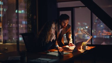 Heyecanlı iş arkadaşları karanlık ofisin kapanışında sevinçle dizüstü bilgisayar izliyorlar. Gece işyerinde iş başarısını kutlayan iki meslektaşınız kutlu olsun. Duygusal partnerlere beş başarı şansı 