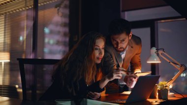 İki iş arkadaşı iş projesinde birlikte çalışıyor. Bu işe dahil olan kadın erkek, akşam ofisinde bilgisayarla başarılı çalışma konusunu tartışıyor. Mutlu meslektaşlar sonuçları kontrol ediyor içerde ortaklığın tadını çıkarıyor