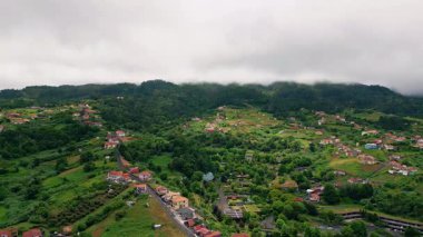 Rural landscape under cloudy sky aerial view. Cozy small village placed in lush greenery gloomy day. Countryside buildings with red rooftops hiding in green nature vegetations. Beautiful scenery.