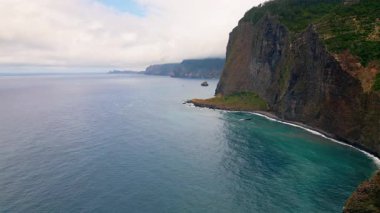 Idyllic lagune cloudy day aerial view. High stone cliff rising over calm deep blue ocean water. Beautiful sea waves meeting dark volcanic rock. Picturesque marine landscape. Peaceful island beauty.