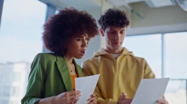 Creative managers watching papers enjoying successful teamwork in light office studio closeup. Happy multiracial colleagues discussing business document. Smiling team working together reading report.