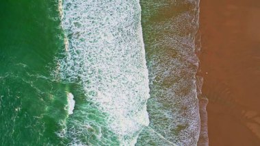 Drone view turquoise sea water foaming on scenic sand beach. Beautiful ocean waves washing empty coast in super slow motion. Top shot white foam crests rolling on tropical shore. Marine landscape.