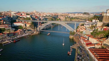 Aerial view Dom Luis bridge crossing Douro river with vessels sailing calmly. Monumental steel construction linking Porto neighborhoods. Scenic panorama urban districts with tiled roofs. Trip concept