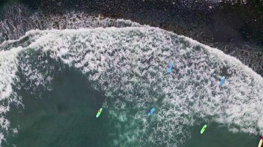 Top view group colorful kayakers floating in foamy ocean waves rolling to dark rocky beach. Aerial shot small boats swimming on deep blue water. Picturesque tide splashing washing beautiful shoreline.