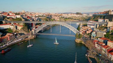 Drone view bridge spanning Douro river in Porto with boats moving below. Architectural structure connecting urban districts under clear sky looking monumental. Aerial beautiful European city landscape