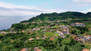 Aerial view red rooftops houses surrounded vivid greenery. Breathtaking countryside landscape summer day. Cozy residential districts in Mediterranean settlement. Green vegetation covering village.