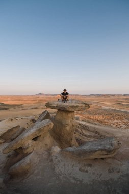 Navarra 'daki Bardenas Reales çölünde gün batımında bir kaya formasyonunda oturan adam.