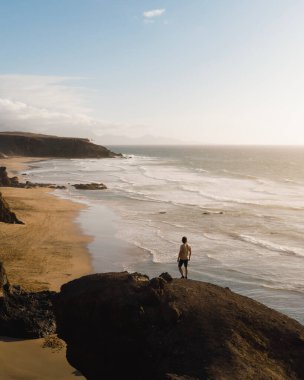 Genç adam gün batımında Fuerteventura kayalıklarından denizi izliyor.
