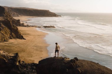 Genç adam Kanarya Adaları 'nı gezerken Fuerteventura sahilinde günbatımının tadını çıkarıyor.