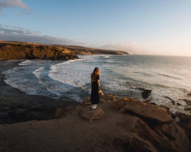 Mujer joven al atardecer ayık un rocoso acantilado de Fuerteventura durante su viaje por las Canarias