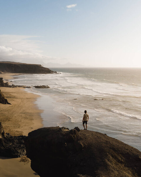 young man watches the sea from some rocky cliffs of fuerteventura at sunset