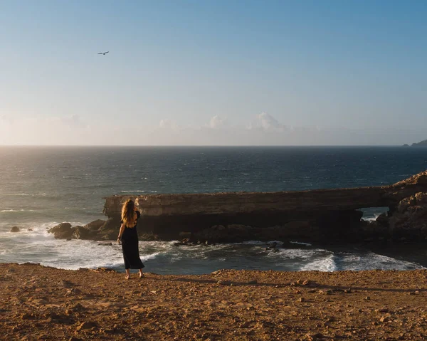 stock image young woman watches the sea from some rocky cliffs of fuerteventura at sunset