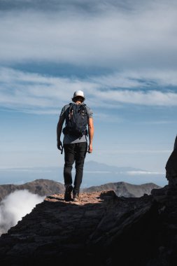 Sırt çantalı genç adam arka planda Tenerife ve Pico Teide adalarıyla La Palma adasındaki Caldera de Taburiente Milli Parkı 'nda yürüyüş yapıyor..