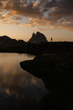 Midi d 'Ossau tepesinin silueti ve sıcak günbatımındaki bir insan Pireneler' de günbatımından önce Anayet göllerine yansıdı.