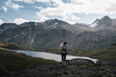 Norveç 'in engebeli dağ manzarasını ve sakin gölü keşfeden dişi yürüyüşçü..