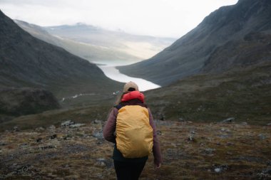 Sarı sırt çantalı bir yürüyüşçü dağlarla çevrili bir Norveç vadisinde yürüyor.