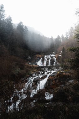 Misty Waterfall in the Pyrenees with Woman standing on a Bridge clipart