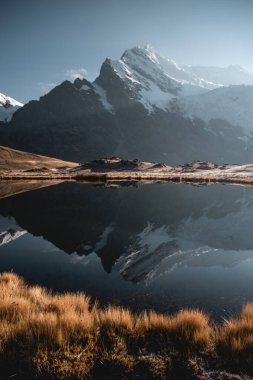 Şok edici gün doğumu And Dağları 'nın karlı tepelerini aydınlatır. Yüksek rakımlı gölün sakin sularında kusursuz bir şekilde yansıtır.