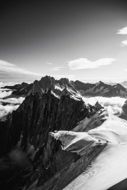 Tepelerden geçen dağcılar, Mont Blanc tepeleri tarafından çerçevelenmiş.