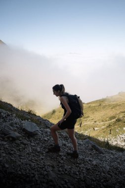 Yürüyüşçü bulutların üstündeki dağlarda kayalık bir patikada yürüyor.