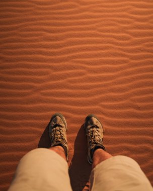 Sahara çölünde, Merzouga, Fas, Afrika yakınlarındaki dalgalı kum tepecikleri üzerinde duran yürüyüş botları giyen bir turist.