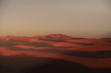 Merzouga, Fas 'taki erg chebbi kumullarının üzerinde güneşin çarpıcı bir şekilde batışı sıcak ve davetkar bir ışık yaratıyor.