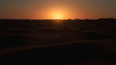 Merzouga yakınlarındaki Erg Chebbi 'nin kum tepelerinin ardında güneş batıyor. Sahara Çölü, Fas' ta güzel bir turuncu parıltı yaratıyor.