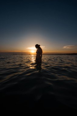 Akdeniz 'in sakin sularında güzel bir günbatımının tadını çıkaran bir kadının silueti.