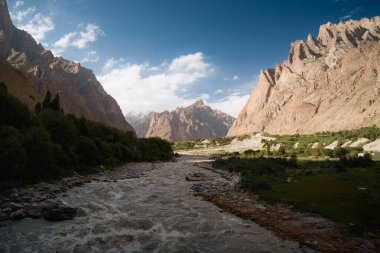 Sükûnet vadisinden akan sakin nehir berrak gökyüzünün altında yükselen dağlarla