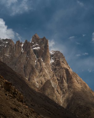 Güneş ışığı, Baltoro Vadisi 'ndeki Karakoram' ın engebeli tepelerini aydınlatarak bulutlu bir gökyüzünün altında dramatik bir manzara yaratıyor.