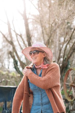 Uluslararası İşçi Bayramı 'nı kutlayan neşeli, kıdemli bir kadın çiftçi güneşli bir meyve bahçesinde hırkasını giyer.