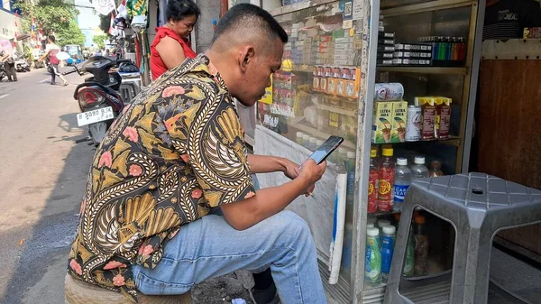 Delikanlı dükkanda cep telefonu kullanıyor.