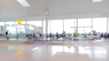 Ağır çekim. Havaalanı terminalindeki bekleme koltuklarının bulanık görüntüsü. Az sayıda yolcu oturmuş ve elektronik araçların yanından geçiyor. Yolcuları alıp götürüyorlar.