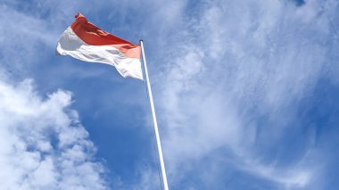 Bulutlu mavi gökyüzünün altında Endonezya Ulusal Bayrağı, Merah Putih 'in alçak açılı görüntüsü. Bayrak, halkının kan ve kemiklerinin rengini sembolize eden kırmızı ve beyaz renklerden oluşur. Boşluk bileşimini kopyala.