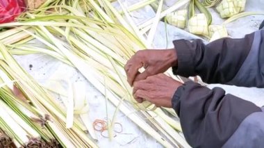 Ağır çekim. Asyalı adamın elleri genç hindistan cevizi yapraklarını ketupata sarma tekniğini gösterdi.. 