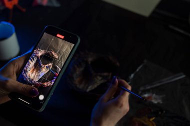 Usta, blogu için akıllı telefon içeriği üzerine bir video çekiyor, bir ejderhanın zanaatını karanlık bir arkaplanda kartonpiyer tekniğini kullanarak bir fırçayla resmediyor. Bir sanat atölyesinde çalışıyorum.