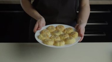 Ev kadınlarının elleri, üzerinde susam tohumları serpiştirilmiş taze, kanlı kurabiyeler bulunan büyük, düz beyaz bir tabak tutuyor. Evde yemek pişirmek, yemek tarifi