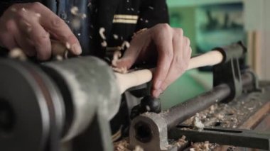 Usta 'nın elleri dönen bir marangoz makinesine bir tahta parçasından bir ürün oyuyor. Demir bir aletin dokunuşuyla talaş ufalanır, yavaş yavaş yakın plan.
