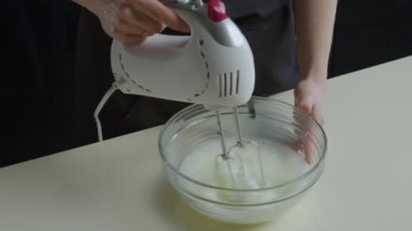 Ev hanımlarının elleri beyaz bir mikser ve şeffaf bir tabak tutuyor, krema için yumurta beyazı çırpıyor. Pişirme işlemi, yavaş pişirme mutfağındaki tarife göre yapılır.