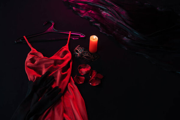 Red satin dress on hanger prepared for date on valentines day lying on black bed near massage candle, mask and rose petals Preparing for a date, flatley