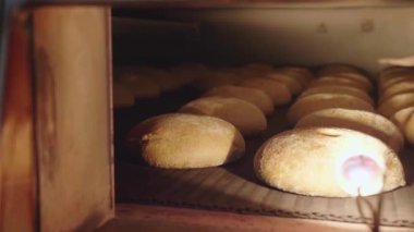 Sıralar halinde dizilmiş pek çok somun ekmek, küçük bir pencereden görülen bir fabrikadaki sanayi fırınında pişiriliyor. Üretimde üretim süreci, yakın plan
