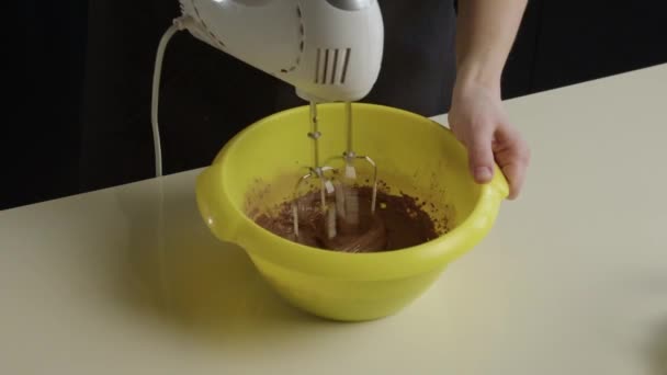 コックの手は チョコレート生地をホイップするミキサーと黄色い深いプラスチックボウルを保持しています ココアでデザートを作るプロセス スローモのクローズアップ — ストック動画
