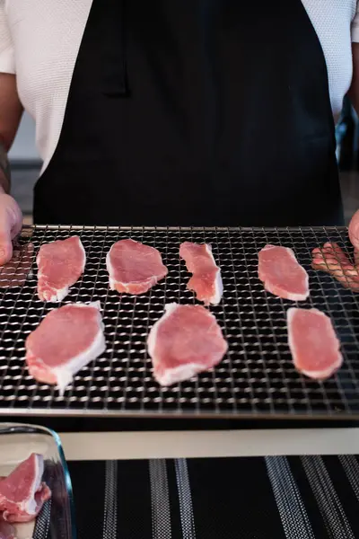 Thinly sliced slices of pickled pork meat are laid out on a metal dehydrator grid. The process of making snacks, close-up, vertically