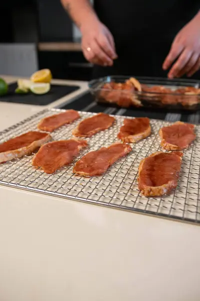 Thinly sliced slices of pickled pork meat are laid out on a metal dehydrator grid. The process of making snacks, close-up, vertically