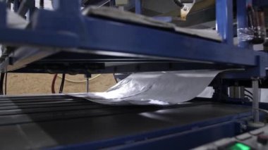 Beyaz bir polietilen un torbası fabrikadaki otomatik mavi kesicinin konveyörüne biner. Malların seri üretim süreci, 4k yakın plan.
