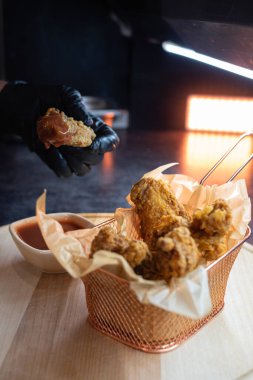 Siyah lateks eldivenli bir el kızarmış tavuk kanadı sepetinden bir tane alıp sosa batırdı. Fast food işletmesi, yemek servisi, dikey olarak yakın çekim.